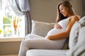 Smiling pregnant woman sitting in sofa looking at her stomach Royalty Free Stock Photo