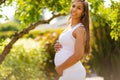 Smiling pregnant woman standing in garden holding hands on belly Royalty Free Stock Photo