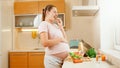 SMiling pregnant woman waiting for baby eating fresh vegetables and looking out of window on kitchen. Concept of healthy Royalty Free Stock Photo