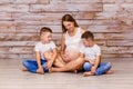 Smiling pregnant woman with two children sitting on the floor on a wooden background in the Studio. family in white t-shirts Royalty Free Stock Photo