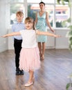 Girl rehearsing curtsey in dance hall with boy partner and female teacher