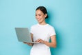 Smiling pretty asian girl in white t-shirt, working on project, looking satisfied and happy at laptop screen Royalty Free Stock Photo