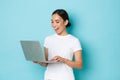 Smiling pretty asian girl in white t-shirt, working on project, looking satisfied and happy at laptop screen Royalty Free Stock Photo