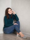 Smiling pretty brunette woman with magnificent eyes and adorable smile in green sweater and blue jeans relaxing sitting on floor Royalty Free Stock Photo