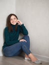 Smiling pretty brunette woman with magnificent eyes and adorable smile in green sweater and blue jeans relaxing sitting on floor Royalty Free Stock Photo