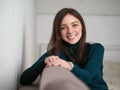 Smiling pretty brunette woman with magnificent eyes and adorable smile in green sweater and blue jeans relaxing sitting on sofa at