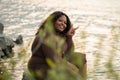 Smiling pretty curly plump multicultural dark skin woman sitting by sea, gesturing, show peace sign. Grass foreground