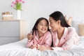 Smiling pretty cute korean millennial woman hugging teenage daughter in pink pajama lie on bed in bedroom