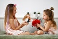 Smiling pretty cute small girls sisters kids with long hair sitting on bed and playing with dolls together