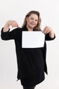 Smiling pretty fat plus-size overweight plump woman in black cardigan holding, pointing finger at blank sheet of paper. Royalty Free Stock Photo