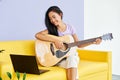 Smiling pretty female learning to play guitar watches a video lesson online using laptop