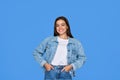 Smiling Latin teen girl wears denim looking at camera stands on blue background. Royalty Free Stock Photo