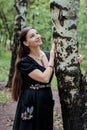 Smiling pretty girl in black Russian dress with embroidery leaned against birch Royalty Free Stock Photo
