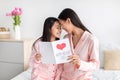 Smiling pretty japanese young female and teen girl in pink pajamas hold card, enjoy time together on bed