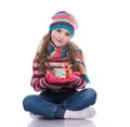 Smiling pretty little girl wearing coloful knitted scarf, hat and gloves, holding christmas gift isolated on white background.