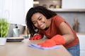 Smiling pretty millennial african american woman in rubber gloves dusting table with dishes