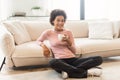 Smiling pretty relaxed millennial african american woman in casual enjoy cup of favorite hot drink, sit on floor