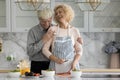Older husband hugs his cheerful wife preparing vegetarian dish