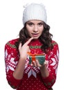 Smiling pretty young woman wearing colorful knitted sweater with christmas ornament and hat, holding christmas gift. Royalty Free Stock Photo