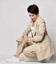 Smiling pretty short haired brunette woman in beige business smart casual suit and skeakers sitting looking at watch