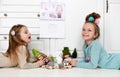 Smiling pretty small girls sisters in home clothes and funny hairstyle with decorations lying on floor and playing dolls toys Royalty Free Stock Photo
