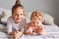 Smiling pretty small kids lying in bed with high spirit enjoying weekend happy little girls playing in bedroom elder sister taking Royalty Free Stock Photo