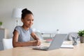 Smiling pretty smart teen african american girl student studying at home, watching online lesson on laptop Royalty Free Stock Photo