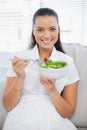 Smiling pretty woman eating healthy salad sitting on sofa Royalty Free Stock Photo