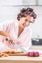 Smiling pretty woman with hair curlers cuts yellow onion on a chopping board in the kitchen