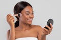 Smiling pretty young african american woman with perfect skin in towel applying powder on face with makeup brush Royalty Free Stock Photo