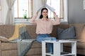 Smiling pretty young Caucasian woman sitting on sofa and holds documents over her head in form of roof. Concept of loan