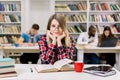 Smiling pretty young female student sitting at table in modern light library room and looking at camera. Books, tablet Royalty Free Stock Photo