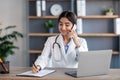 Smiling pretty young hindu woman doctor in white coat with stethoscope talk with patient by phone, works in office Royalty Free Stock Photo