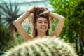 Smiling pretty young woman standing near the cactus and holding her hair Royalty Free Stock Photo