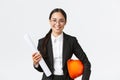Smiling professional asian female architect in business suit and glasses, carry blueprints of home design and safety