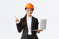 Smiling professional asian female engineer or architect at construction, wearing safety helmet and suit, pointing finger Royalty Free Stock Photo