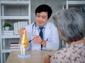 Smiling professional Asian man orthopedic doctor in white suit pointing to knee joint anatomy model. Royalty Free Stock Photo