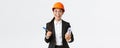 Smiling professional female architect, asian engineer in helmet and business suit, holding blueprints and pen, siging