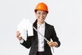 Smiling professional female asian engineer, architect in helmet and business suit showing house maket and tape measure