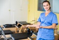 Smiling female physiotherapist inviting to rehab center with pilates equipment