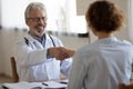 Smiling professional physician handshaking female patient at medical consultation