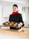 Proffesional woman in chef uniform holding sheet pan with just baked cupcakes