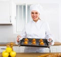 Proffesional woman cook in white uniform holding sheet pan with just baked cupcakes