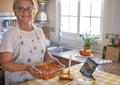 Happy senior woman shows a pan with homemade stuffed cannelloni ready for the oven. Ingredients around her Royalty Free Stock Photo