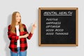 Smiling psychologist standing near board with text, Mental Health.