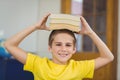 Smiling pupil balancing books on head in a classroom