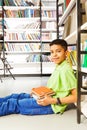 Smiling pupil with pile of books sitting on floor