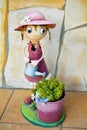 Smiling puppet made in colorful steel that shows a happy cross-eyed girl watering can a bucket with a green plant on a yellow Royalty Free Stock Photo