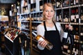 Smiling qualified mature saleswoman offering natural wines in bottles for sale at winery