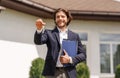 Smiling real estate agent holding house key near new residence to sale, outdoors